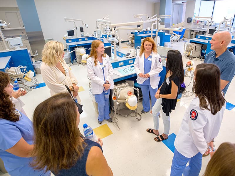 Ashley Porter, in white coat at left, and Bailey Beard Jones, in white coat at right, are starting their final year in the dental hygiene program. They talk with new hygiene students and their parents during Family Day.